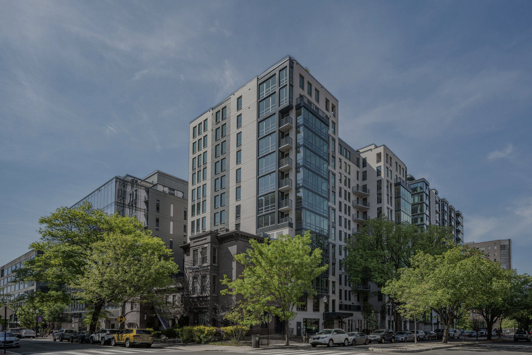 Mount Vernon Triangle, Washington, DC, Luxury Apartments Near Georgetown University Law Center - Claret - Building Exterior Of A Multi-Story Building With Glass Windows, Balconies, And Lush Trees.